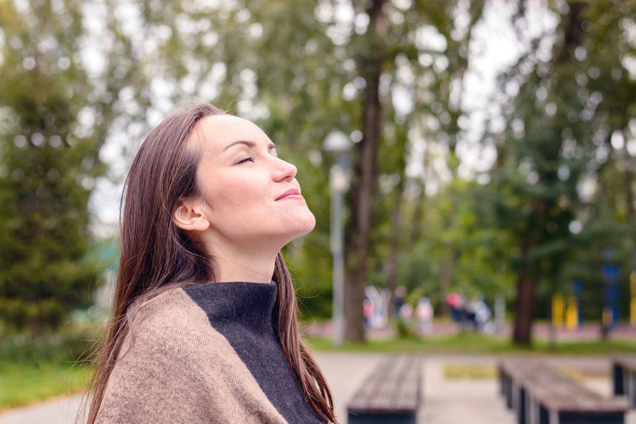 Mlada žena u parku zatvorenih očiju praktikuje vežbe disanja