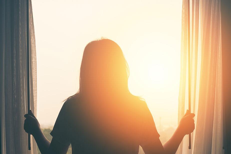 Žena otvara prozor a jutarnje sunce daje samo obrise njenog tela.