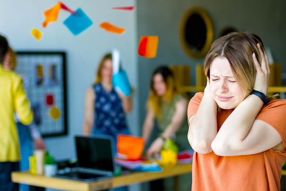 Žena se drži za glavu, prekrila je rukama uši i zatvorila oči jer joj smeta buka iz pozadine