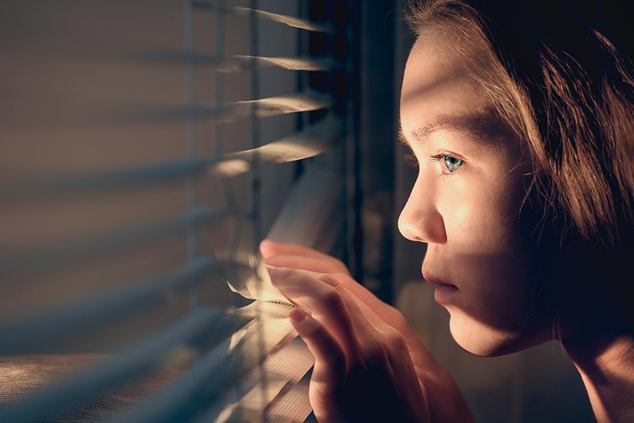 devojka koju muči agorafobija gleda kroz razmaknute venecijanere