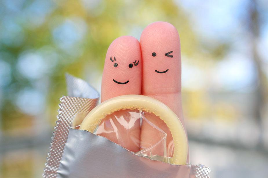 dva prsta sa ljudskim likovima drže kondom - polne bolesti