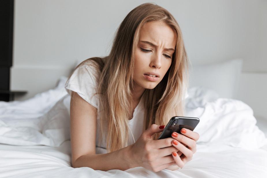 Mlađa devojka leži na stomaku u postelji i gleda u mobilni telefon - Mobilni telefoni i zdravlje