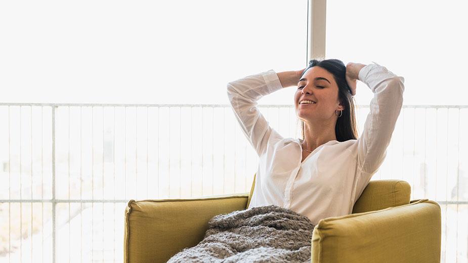 mlađa žena u fotelji sa ćebetom preko nogu i osmehom posle popodnevnog odmora