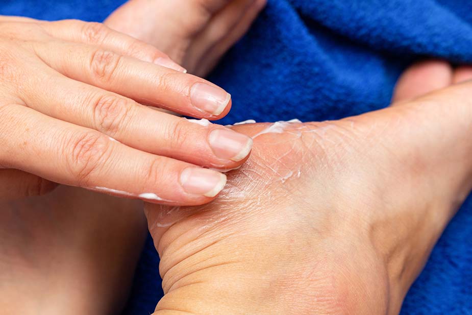 Ženska ruka razmazuje kremu za negu po stopalima