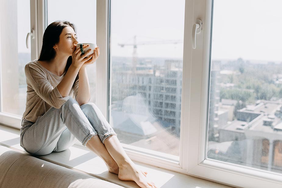 Mlađa žena pije kafu sedeći pored prozora - da li je kafa dobra za zdravlje?