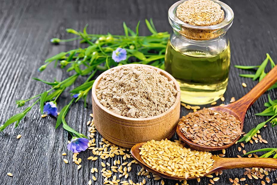 Posuda sa mlevenim lanenim semenom, bočica sa lanenim uljem i dve drvene kašike sa lenenim semenom na stolu
