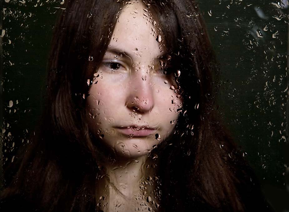 Tužna mlađa žena gleda kroz kišom okupan prozor