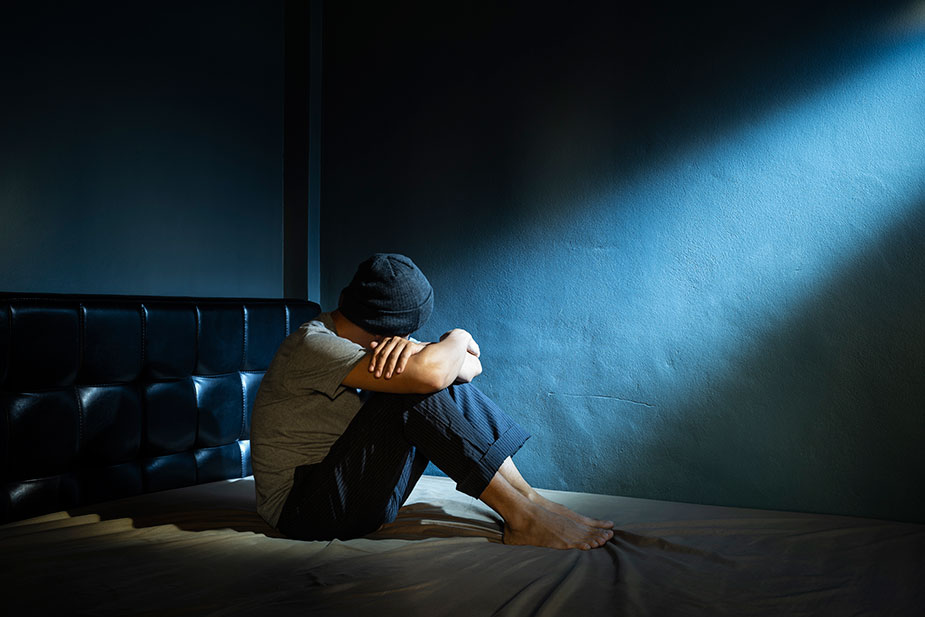 Mladić na krevetu sedi savijenih kolena i pognute glave